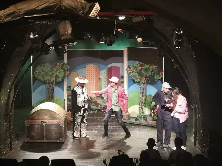 A community-theatre scene in front of a painted backdrop
